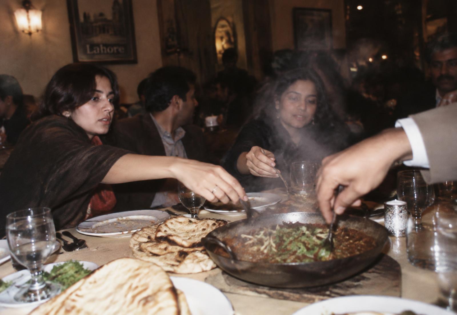 Hands reaching across a shared table for a steaming dish